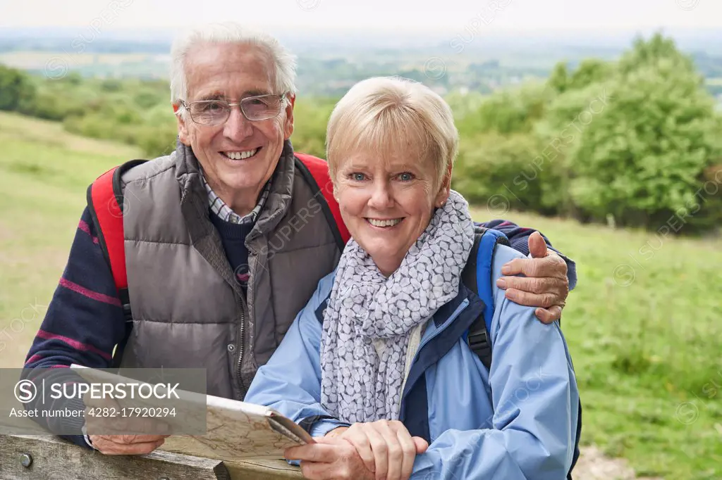 Portrait Of Retired Couple On Walking Holiday Resting On Gate With Map                             