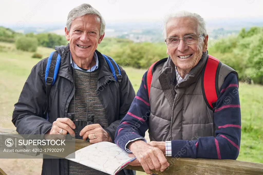 Portrait Of Two Retired Male Friends On Walking Holiday Resting On Gate With Map                             