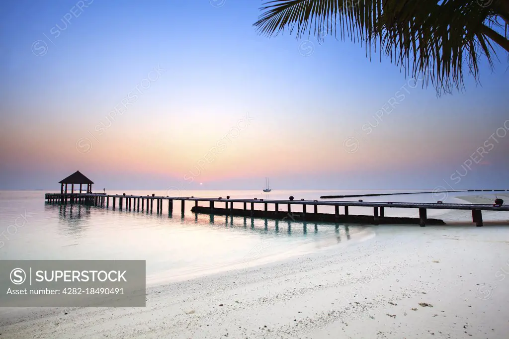 Sunrise over a jetty on an empty tropical beach.