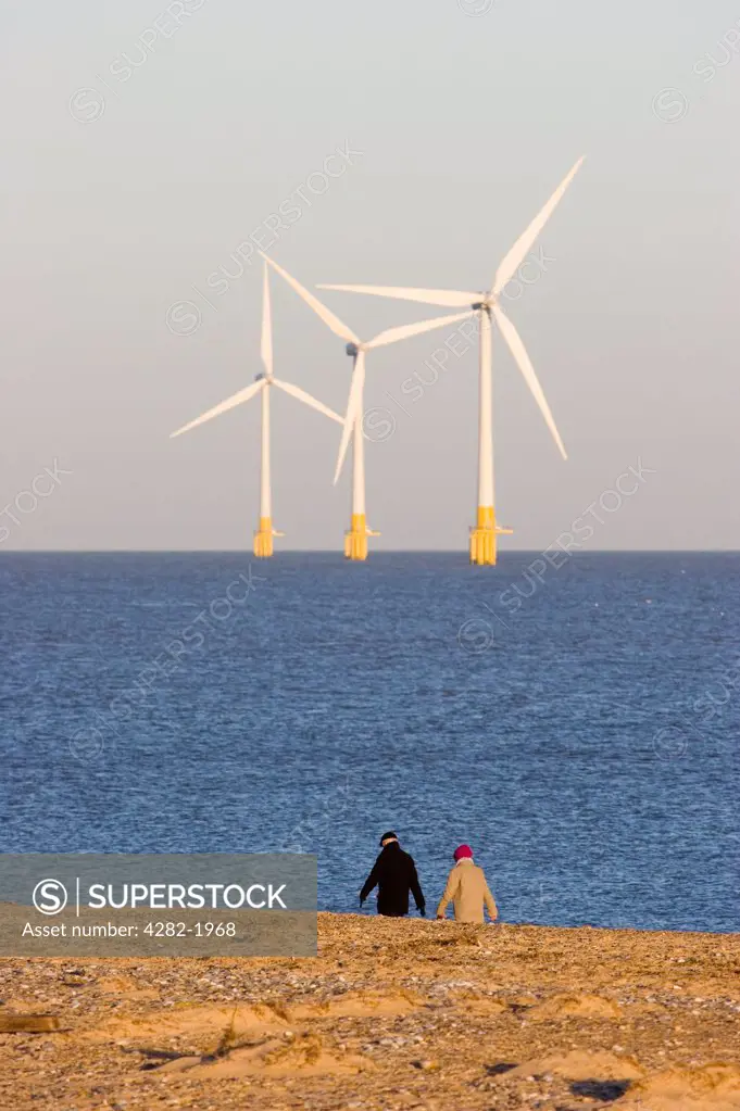 England, Norfolk, Great Yarmouth . Offshore wind farm with couple walking along the foreshore in Great Yarmouth.