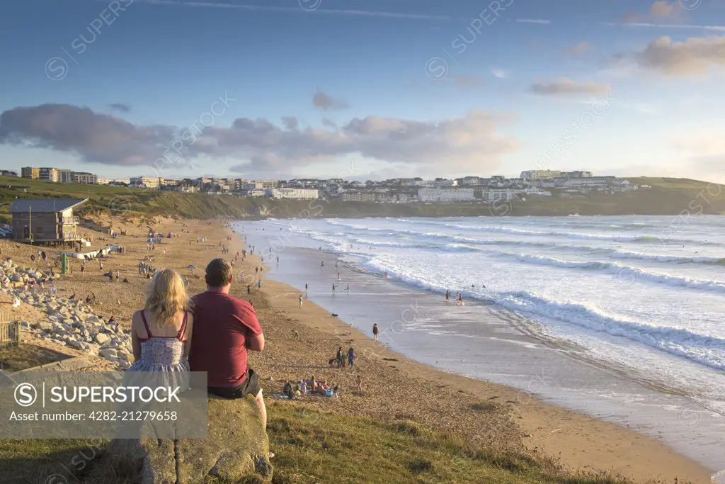 Two holidaymakers sit on a rock and enjoy the sunset over Fistral Beach in Newquay in Cornwall.