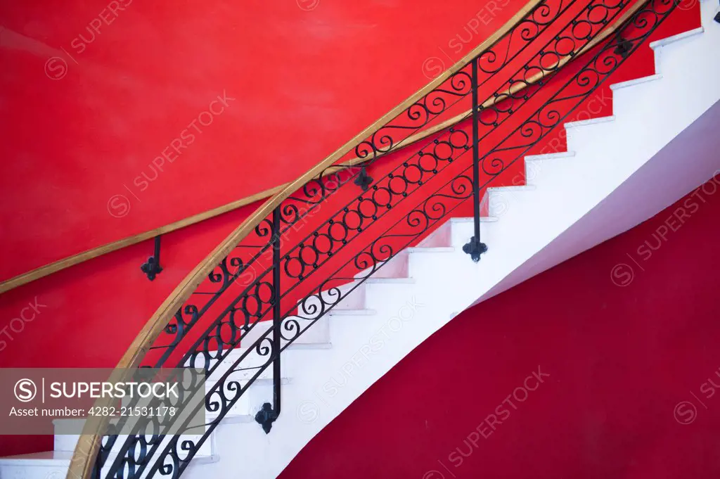 White sweeping staircase set against a red wall in Havana.