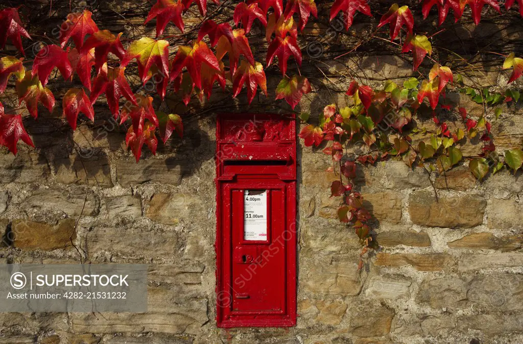 Red post box in wall with autumnal colours.