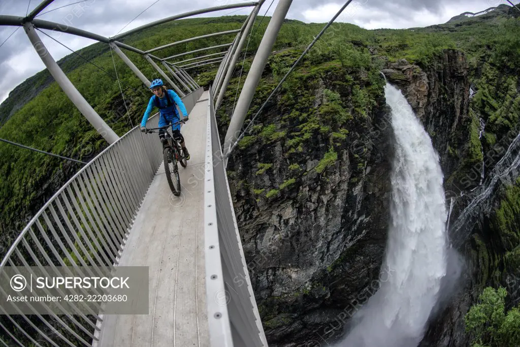 A man rides a mountain bike across the Gorsa Bridge over the Gorza canyon and Gorzi Waterfall in Lyngenfjord in Northern Norway during the summer months.