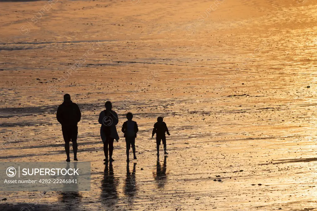A family seen in silhouette walking across Fistral Bech at sunset in Newquay in Cornwall.
