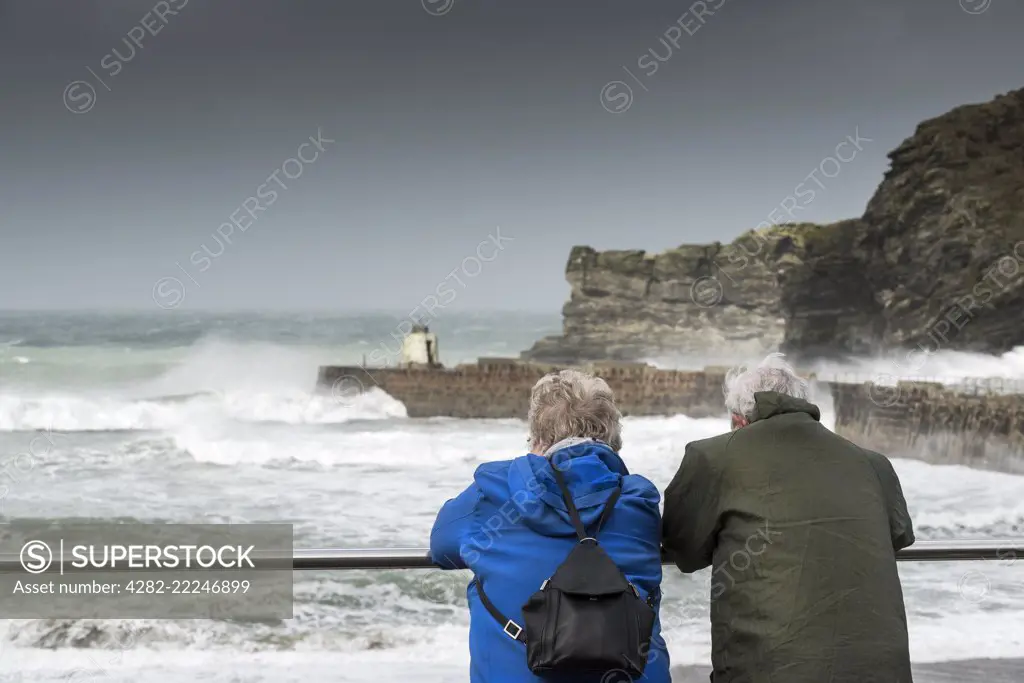 A mature couple watching the rough sea at Portreath in Cornwall.