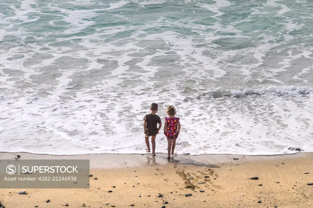 Two young children paddling in the sea at Fistral Beach in Newquay in Cornwall.