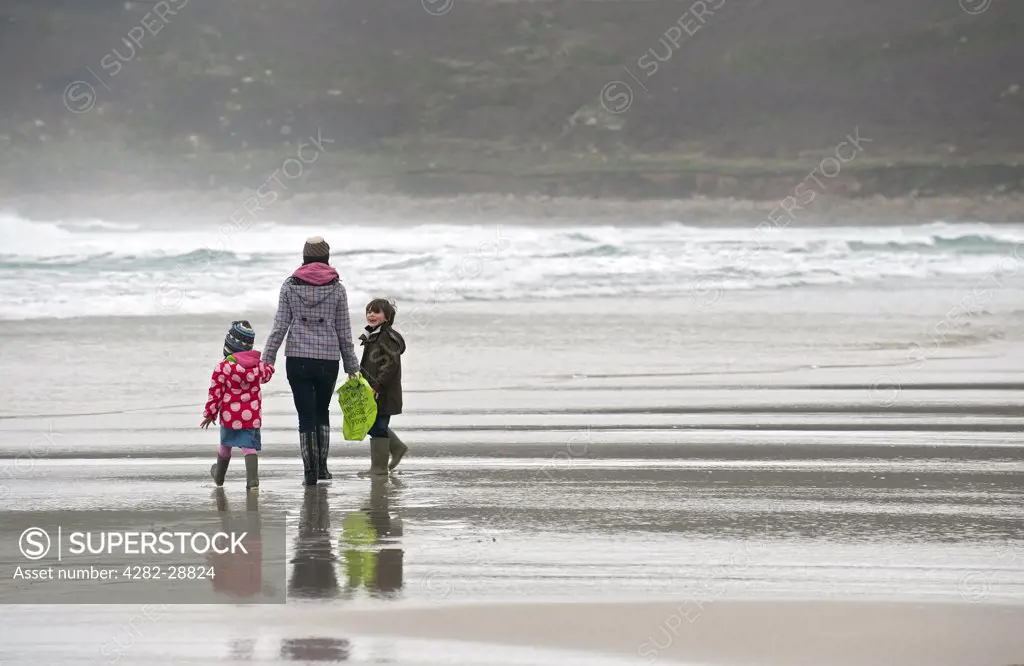 England, Cornwall, Sennen. A mother and her two young children walking along the shore of Sennen Beach.