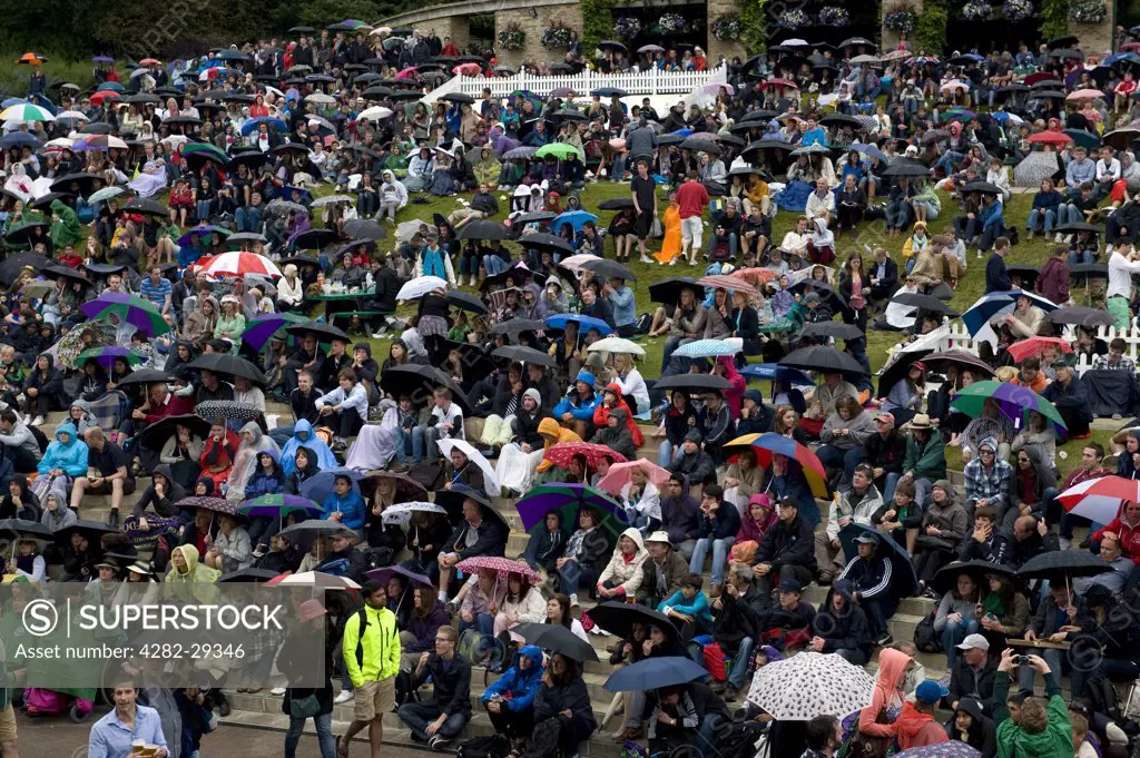 England, London, Wimbledon. Crowds sitting under umbrellas watching the big screen on Aorangi Terrace (Henman Hill) in the rain at the 2011 Wimbledon Tennis Championships.