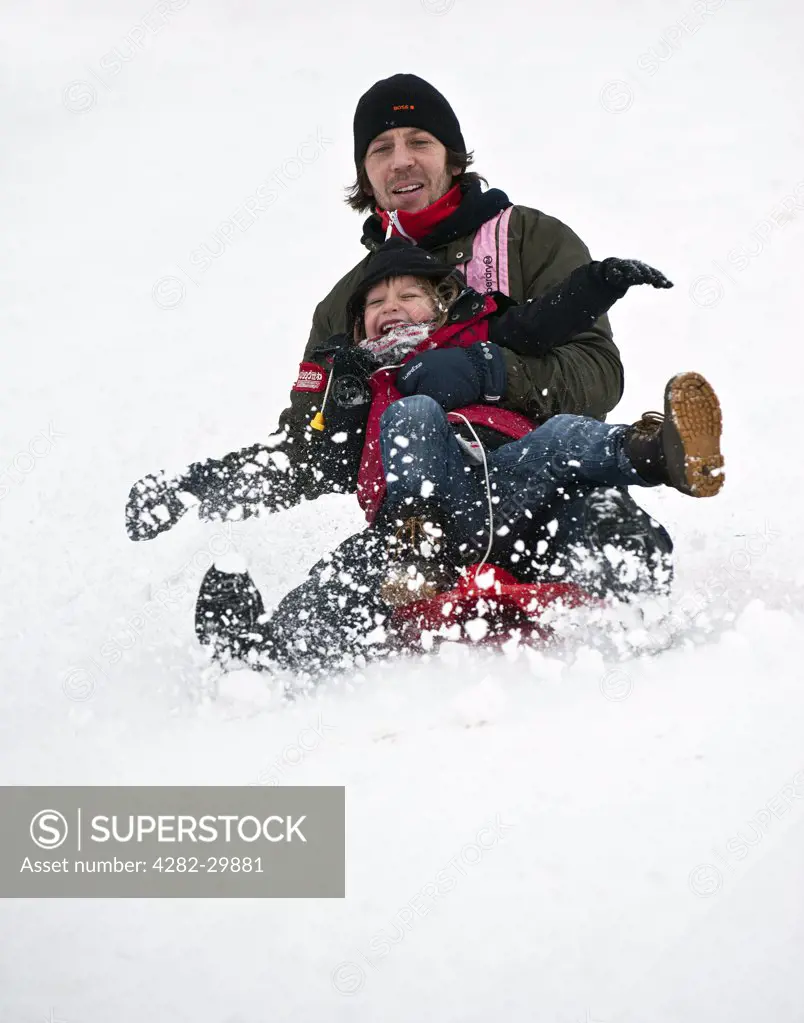 England, Essex, Basildon. Father and child tobogganing in the snow.