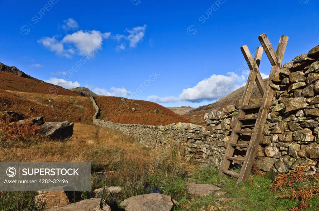 England, Cumbria, Derwent. A stone wall leads from a wooden stile to the hills beyond.