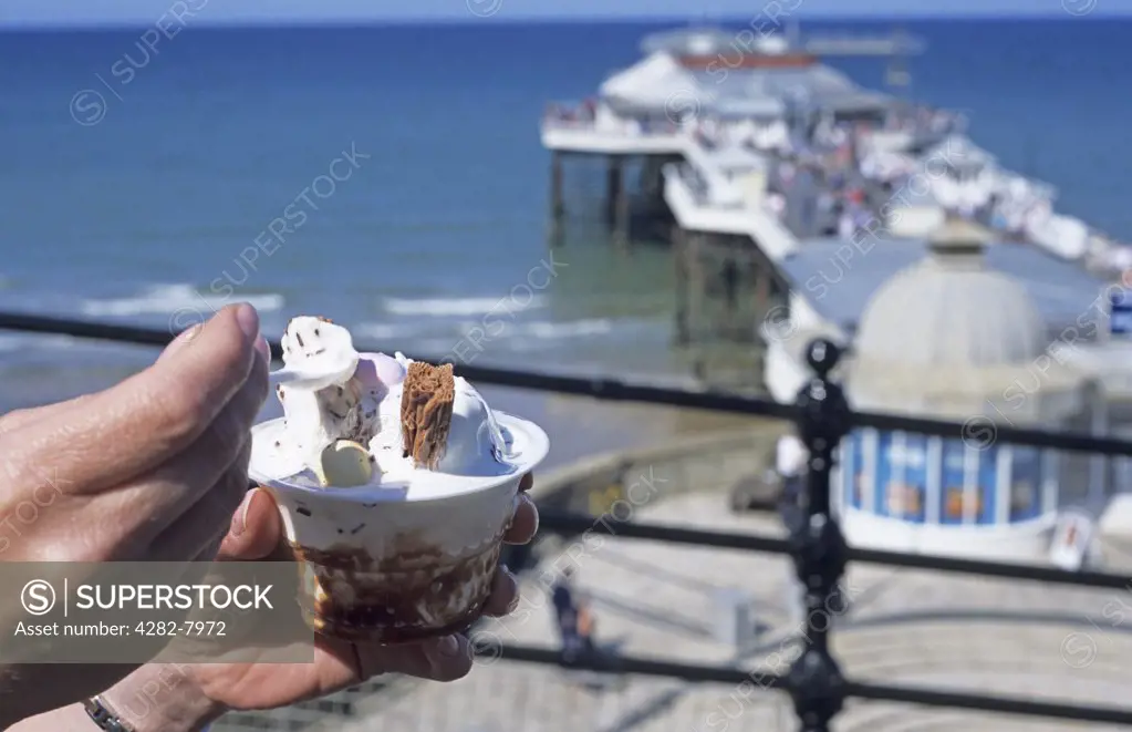 England, Norfolk, Cromer. Enjoying an ice cream overlooking Cromer pier.