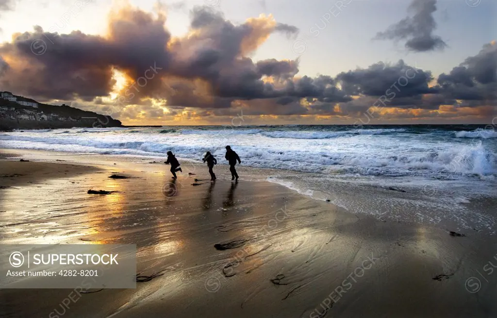 England, Cornwall, Sennen. Three children play on the beach under a dramatic sky at Sennen Cove.