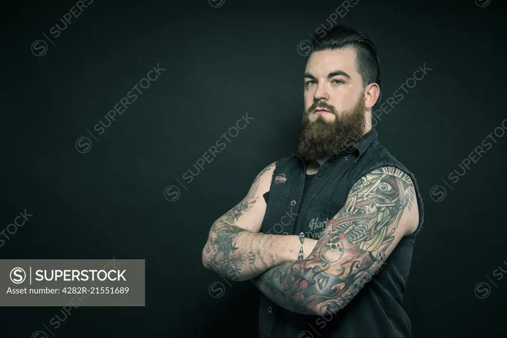 Studio portrait of a bearded man with tattooed arms.