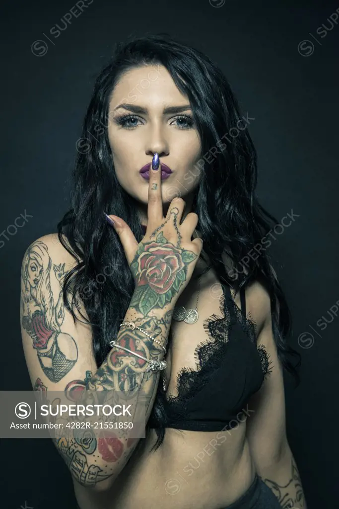 Studio portrait of a young woman with tattooed arms.