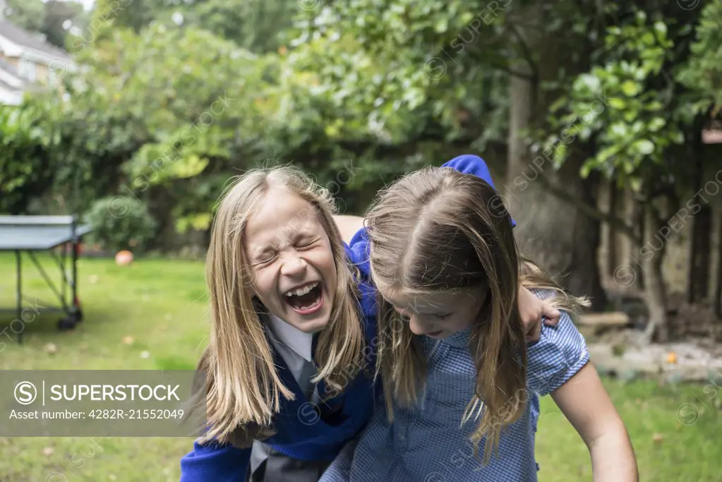 Two ten year old girls in school uniform laughing together outside.