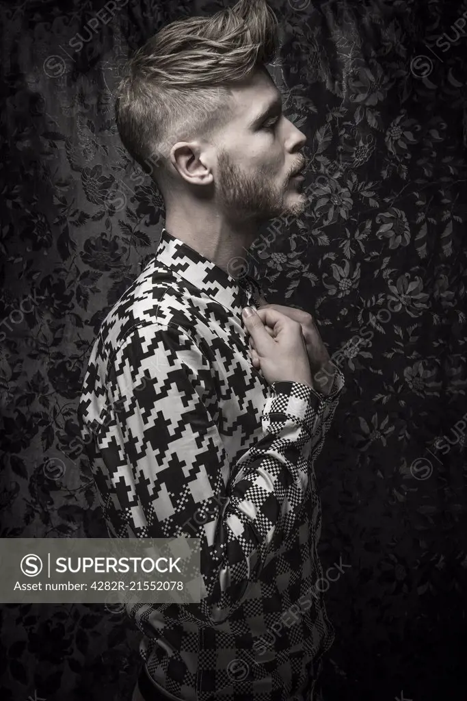 Studio portrait of a bearded young man in a black and white shirt.