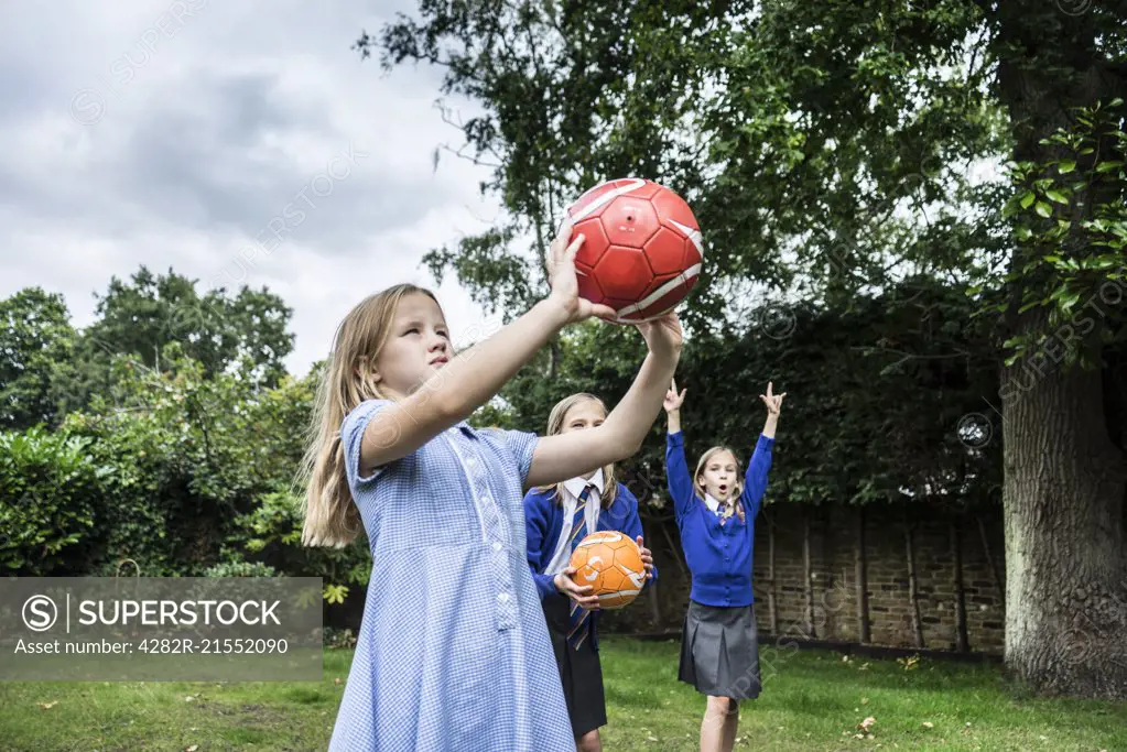 Three girls in school uniform playing with footballs outside.