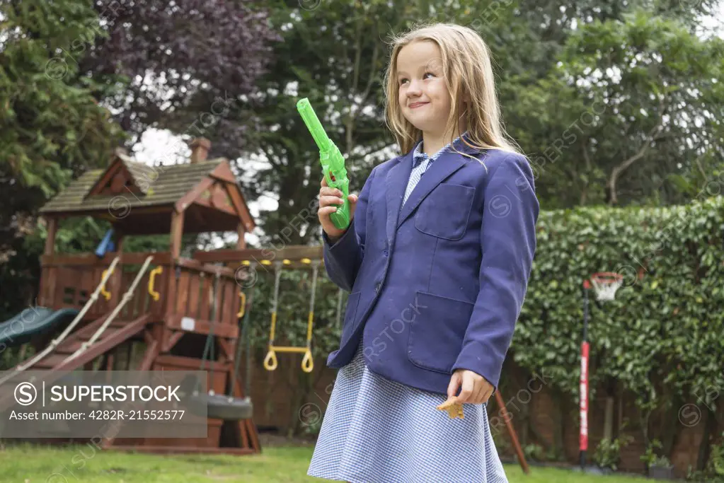 A ten year old girl in school uniform holding a water pistol.