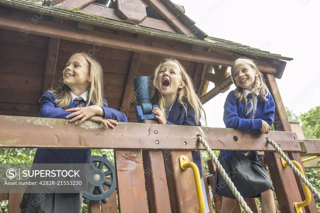 Three girls in school uniform stand together on wooden playground apparatus.