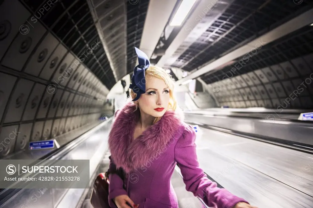 A stylish young woman dressed in 1930s style clothing on a London Underground escalator.