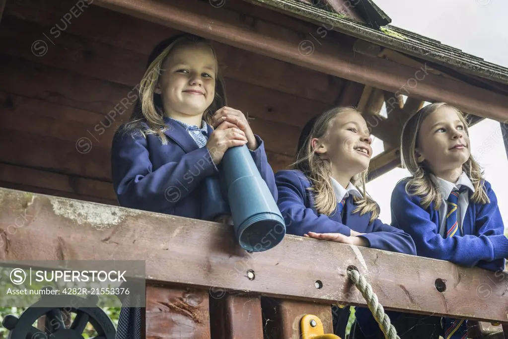 Three girls in school uniform stand together on wooden playground apparatus.