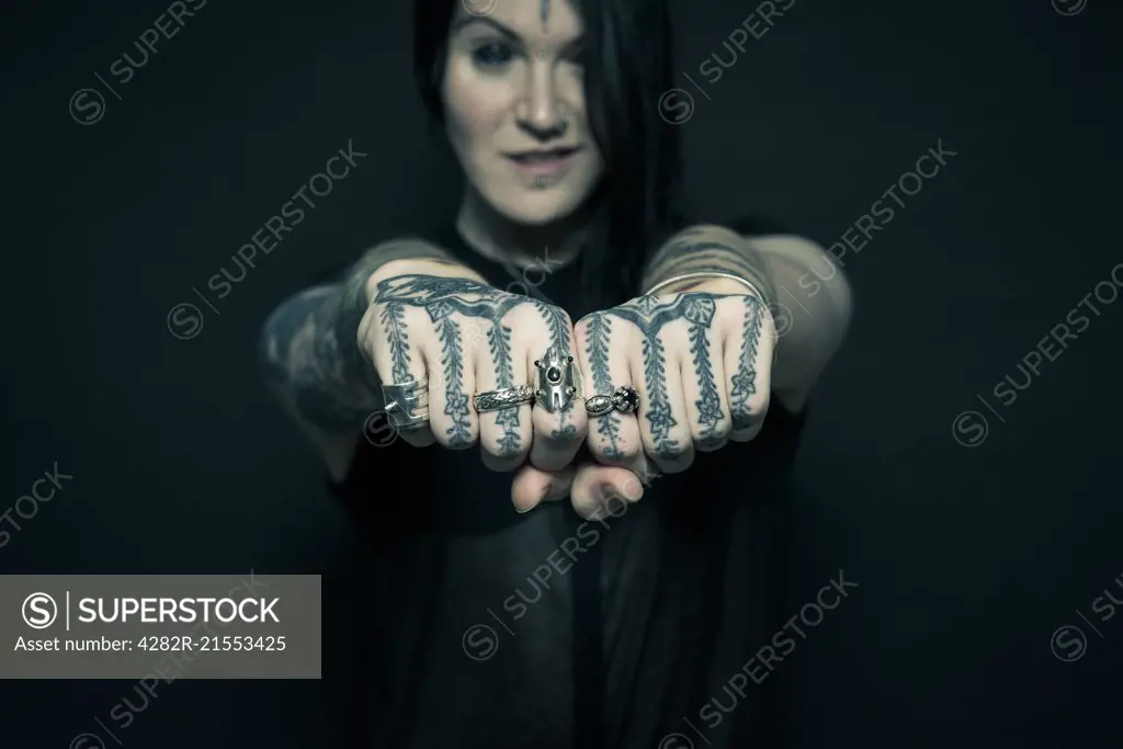 Studio portrait of a young woman with tattooed arms and face.