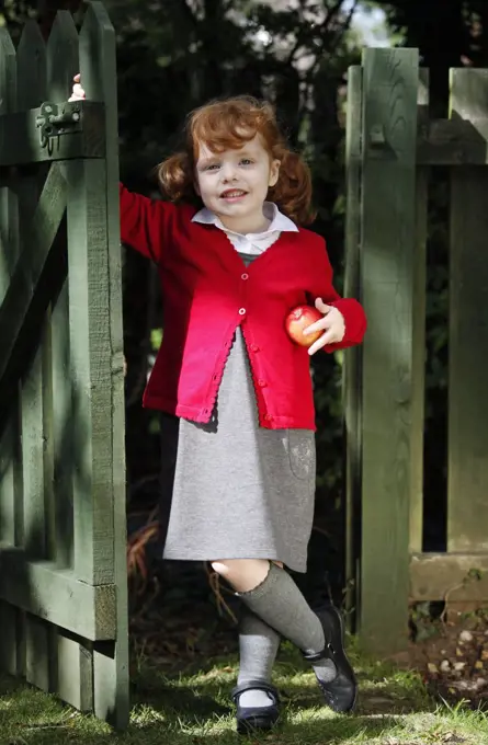 England. A young girl wearing school uniform holding an apple.