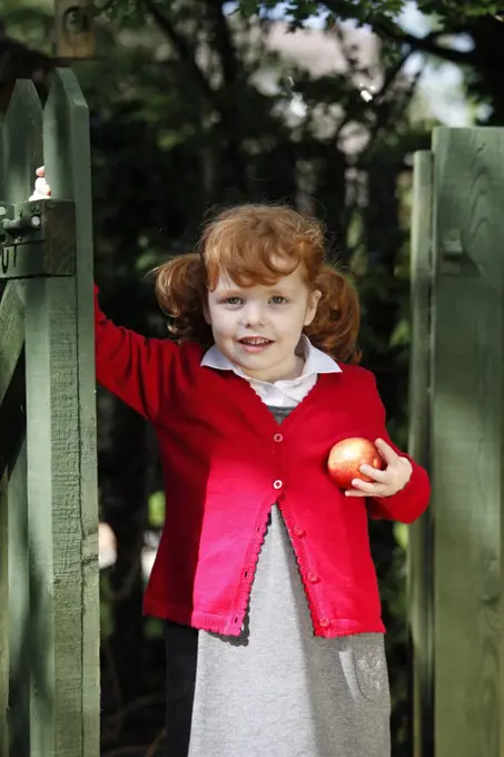 England. A young girl wearing school uniform holding an apple.