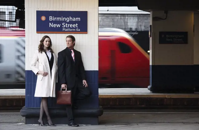 England, West Midlands, Birmingham. A business man and woman standing on a platform at Birmingham New Street station waiting for a train.