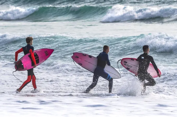 Surfers carrying their surfboards and running into the sea at Fistral in Newquay in Cornwall.