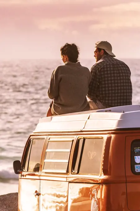 A couple sitting on top of their Volkswagen Campervan enjoying the evening light at Fistral in Newquay in Cornwall.