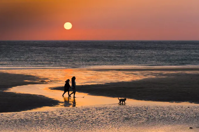 People seen in silhouette at sunset on Fistral Beach in Newquay in Cornwall.