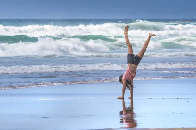 A young teenage girl performing a handstand on the shoreline on Fistral Beach in Newquay in Cornwall.