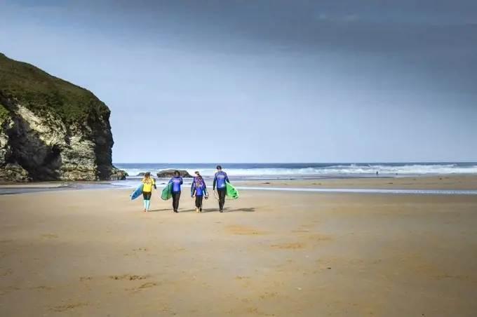 A group of surfers and their instructor carrying their surfboards on Mawgan Porth Beach on the North Cornwall coast.