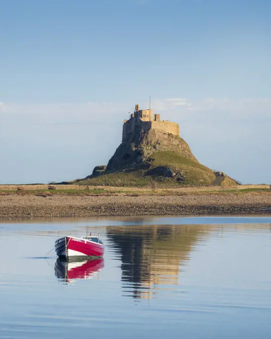 A small red boat in front of Lindisfarne castle reflecting in the sea.