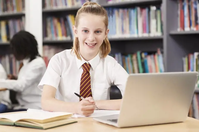 Portrait Of Female High School Student Wearing Uniform Working At Laptop In Library