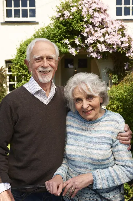 Retired Couple Standing Outside Pretty Home 