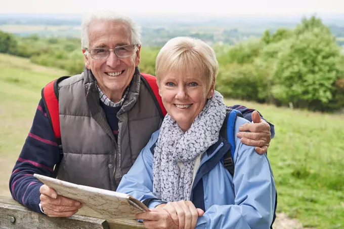Portrait Of Retired Couple On Walking Holiday Resting On Gate With Map                             