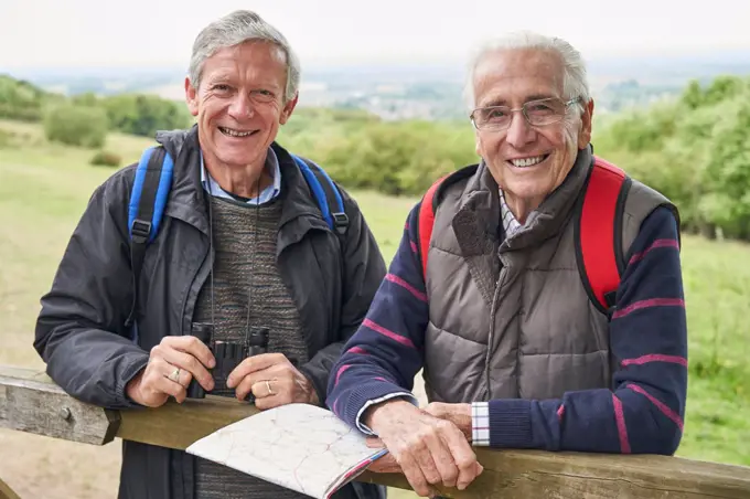Portrait Of Two Retired Male Friends On Walking Holiday Resting On Gate With Map                             