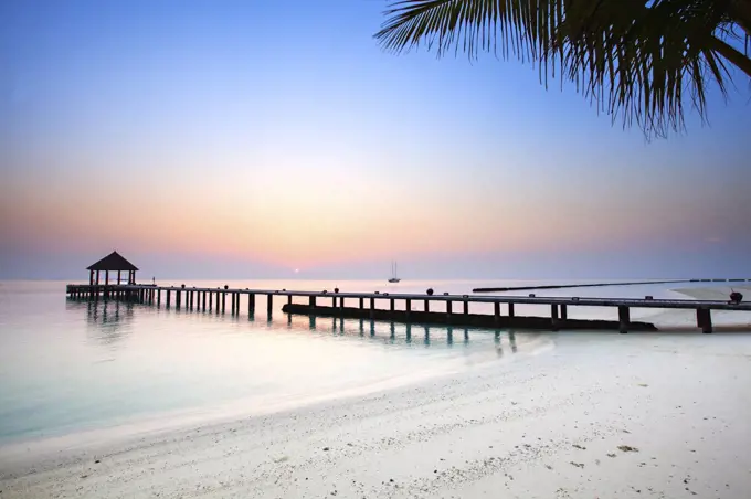 Sunrise over a jetty on an empty tropical beach.