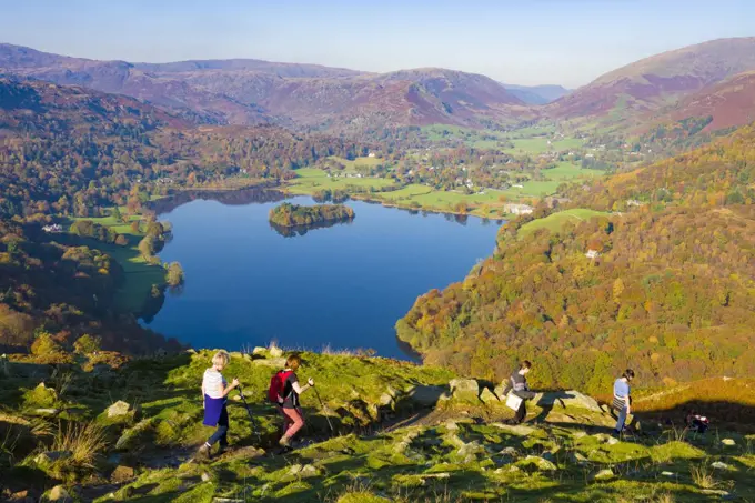 Walkers descending the north western slope of Loughrigg Fell in the Lake District with Grasmere lake beyond.