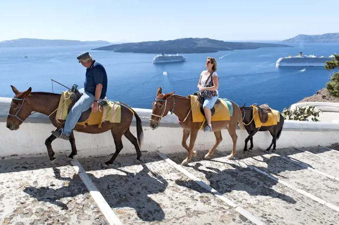 Tourist riding a donkey up the steps leading from the old port to the village of Fira on the Greek island of Santorini.