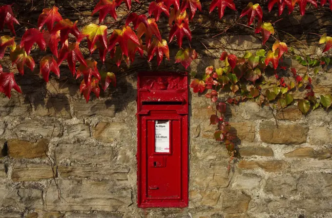 Red post box in wall with autumnal colours.