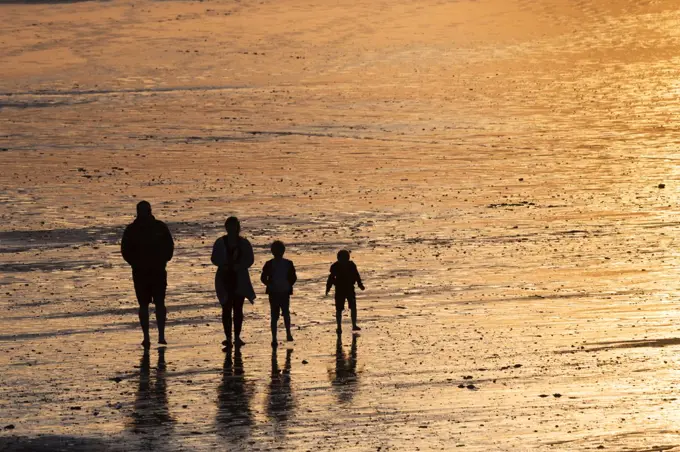 A family seen in silhouette walking across Fistral Bech at sunset in Newquay in Cornwall.