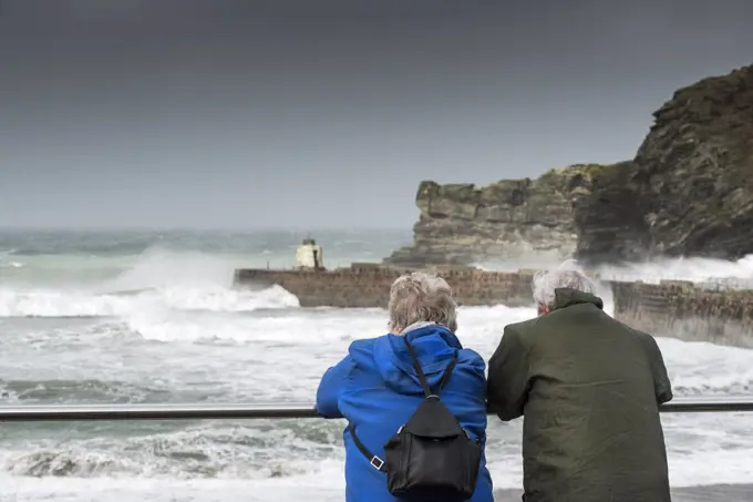 A mature couple watching the rough sea at Portreath in Cornwall.