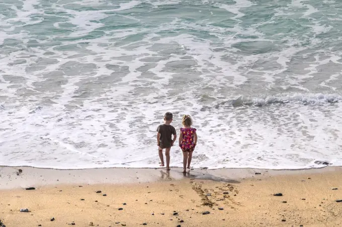 Two young children paddling in the sea at Fistral Beach in Newquay in Cornwall.