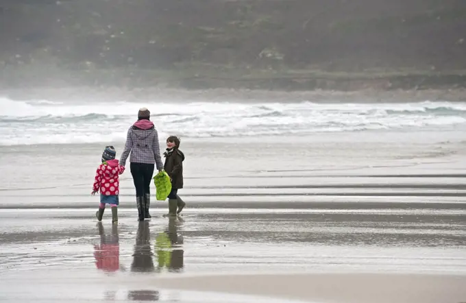 England, Cornwall, Sennen. A mother and her two young children walking along the shore of Sennen Beach.