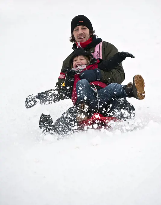 England, Essex, Basildon. Father and child tobogganing in the snow.