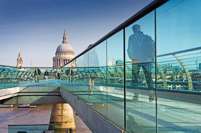 England, London, Millenium Bridge. View of St Paul's Cathedral through glass railings of the Millenium bridge with pedestrians.